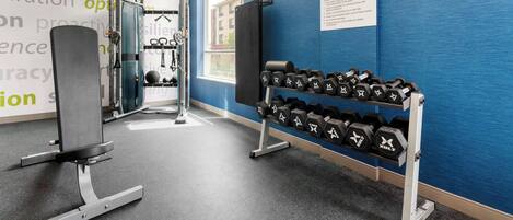 A gym with weightlifting equipment, dumbbells, and a TV mounted on the wall.