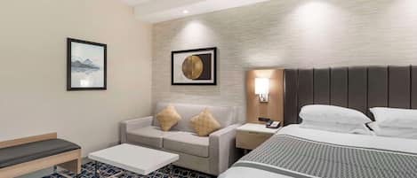Habitación de hotel con cama, sofá, una mesita y dos mesitas de noche.