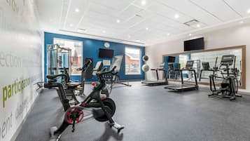 Un gimnasio con diversos equipos de ejercicio, incluyendo cintas de correr y bicicletas estáticas, y un amplio ventanal que proporciona luz natural.