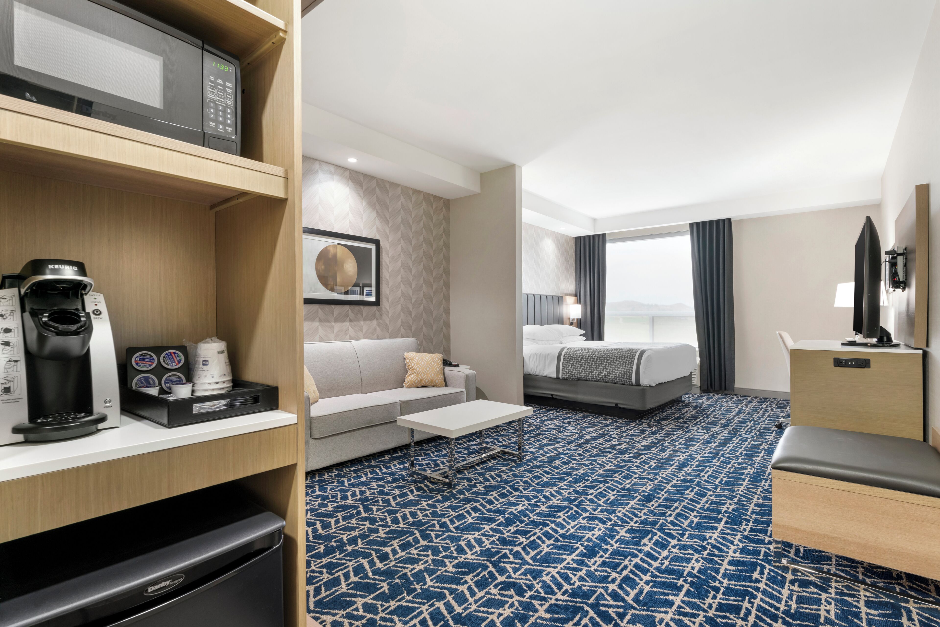 A hotel room with a kitchenette, a sofa, a bed, a TV, and a view of the mountains.