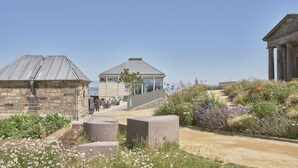 Un bâtiment situé sur la côte, doté d’une façade en pierre, d’une structure moderne en verre et d’un bâtiment classique orné de colonnes.