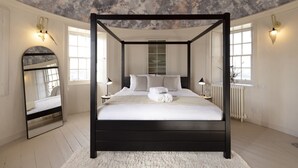 Un lit à baldaquin dans une pièce dotée d’un plafond rustique, de murs blancs et d’un grand miroir sur l’un des murs.