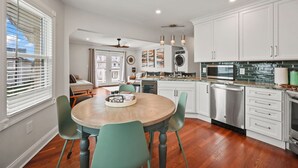 Una cocina moderna con armarios blancos, electrodomésticos de acero inoxidable y una mesa de comedor redonda de madera con sillas color turquesa.