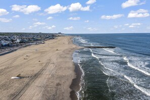 Una playa con un muelle, una orilla arenosa y una zona residencial al fondo.