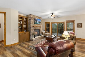 Una sala de estar con chimenea de piedra, muebles de cuero y un ventanal con vista a una terraza.