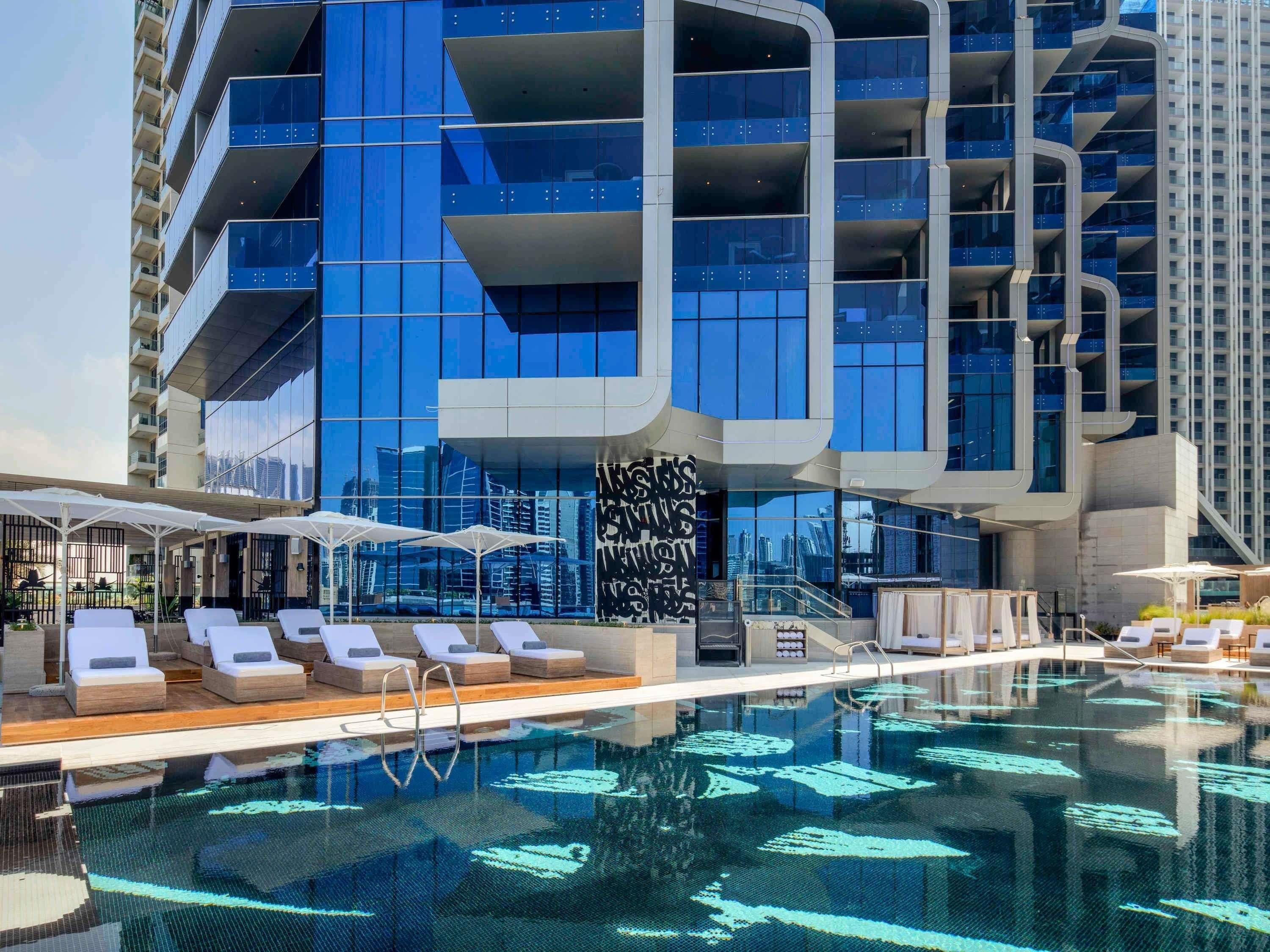 A modern hotel with a rooftop infinity pool, lounge chairs, and a view of the city skyline.