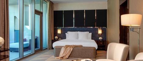 A hotel room with a large bed, a seating area with a table, and a view through floor-to-ceiling windows.