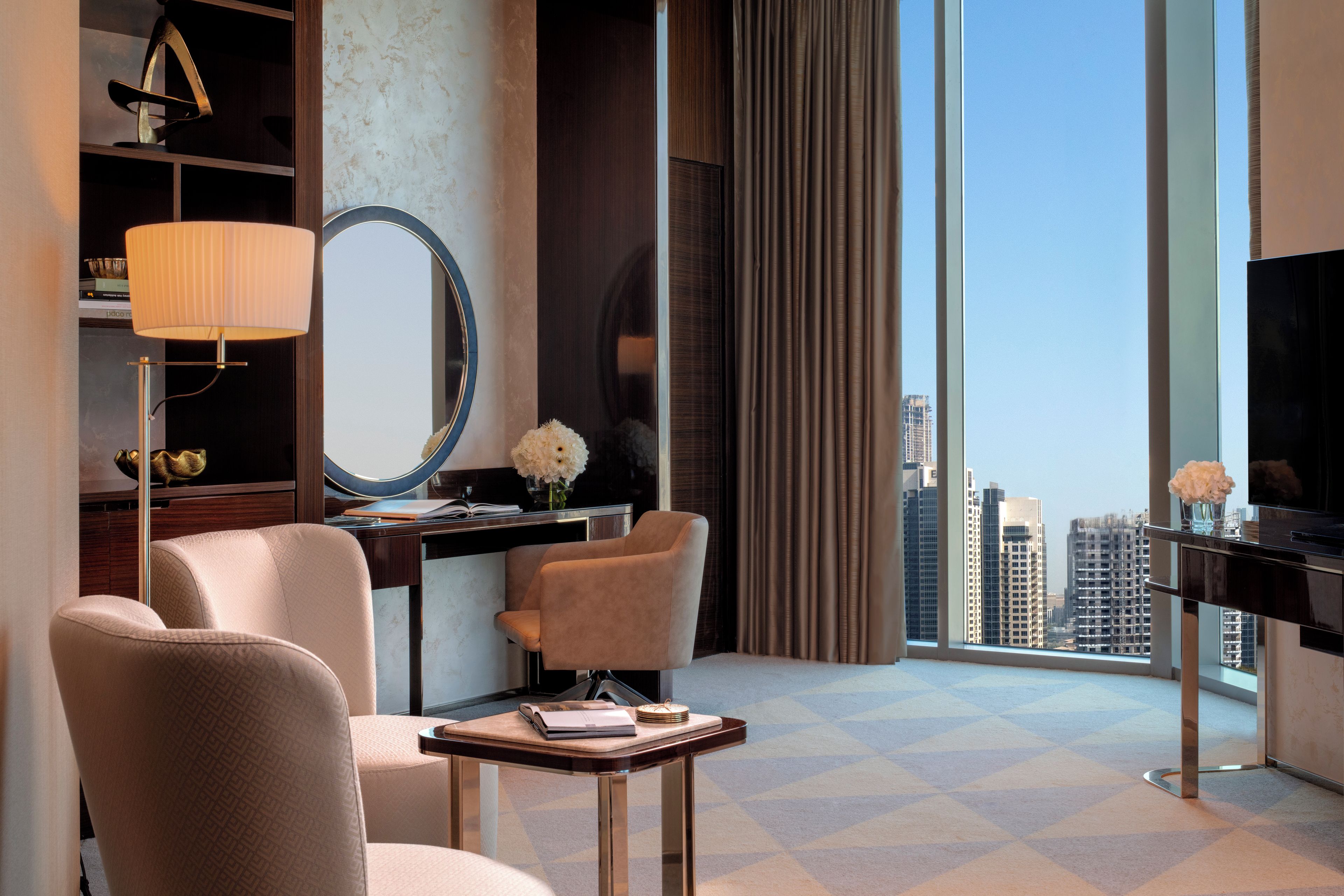 A hotel room with a large window, a desk, a chair, a television, and a mirror.