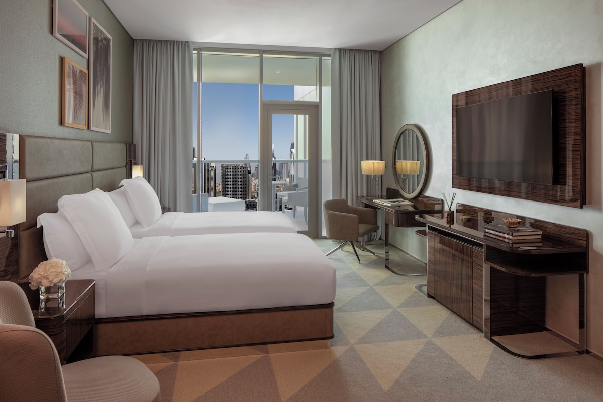 A hotel room with a bed, a desk, a chair, a TV, and a view of the city.