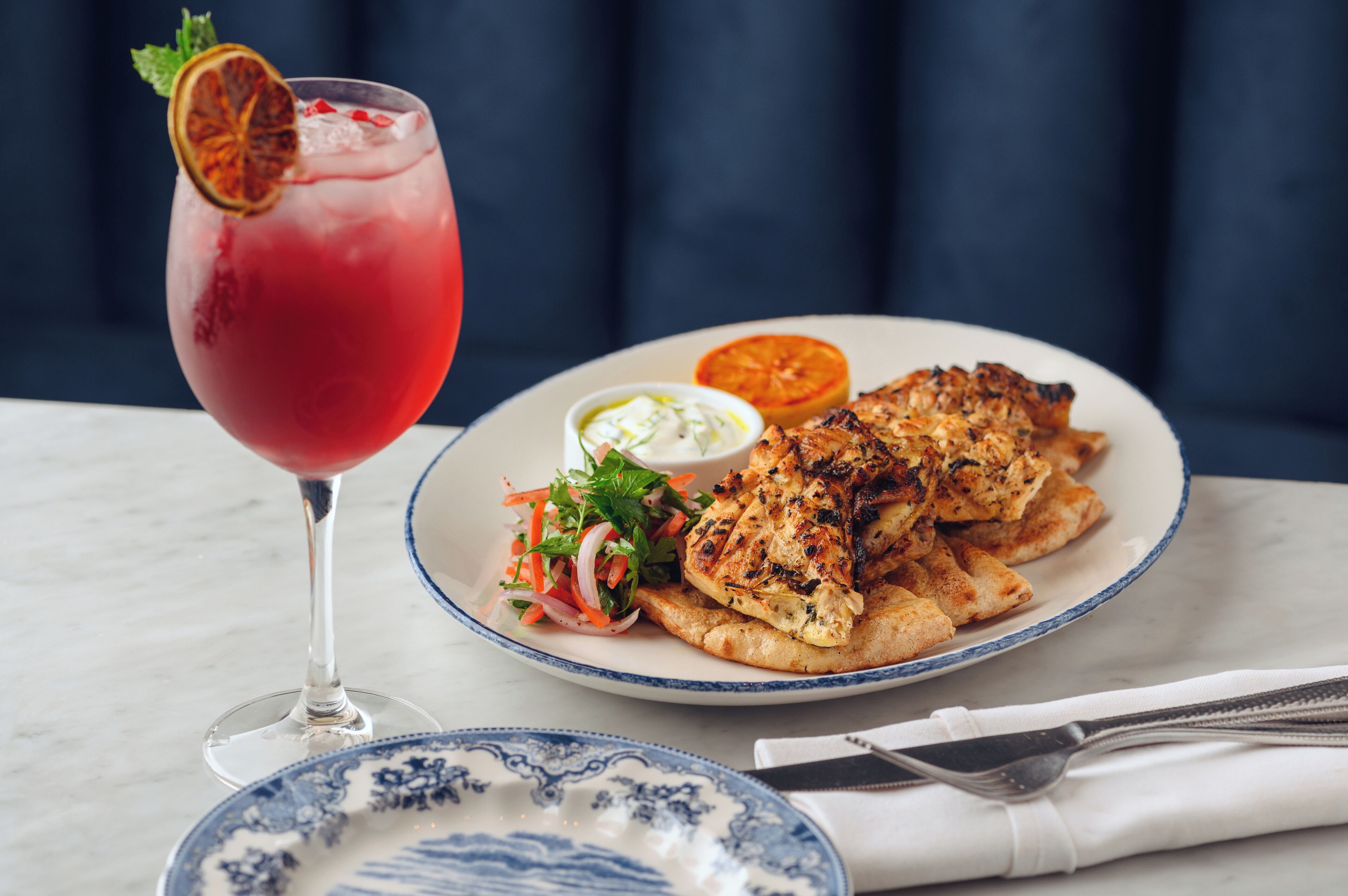 A plate of grilled chicken with a side salad and a glass of red drink on a table.