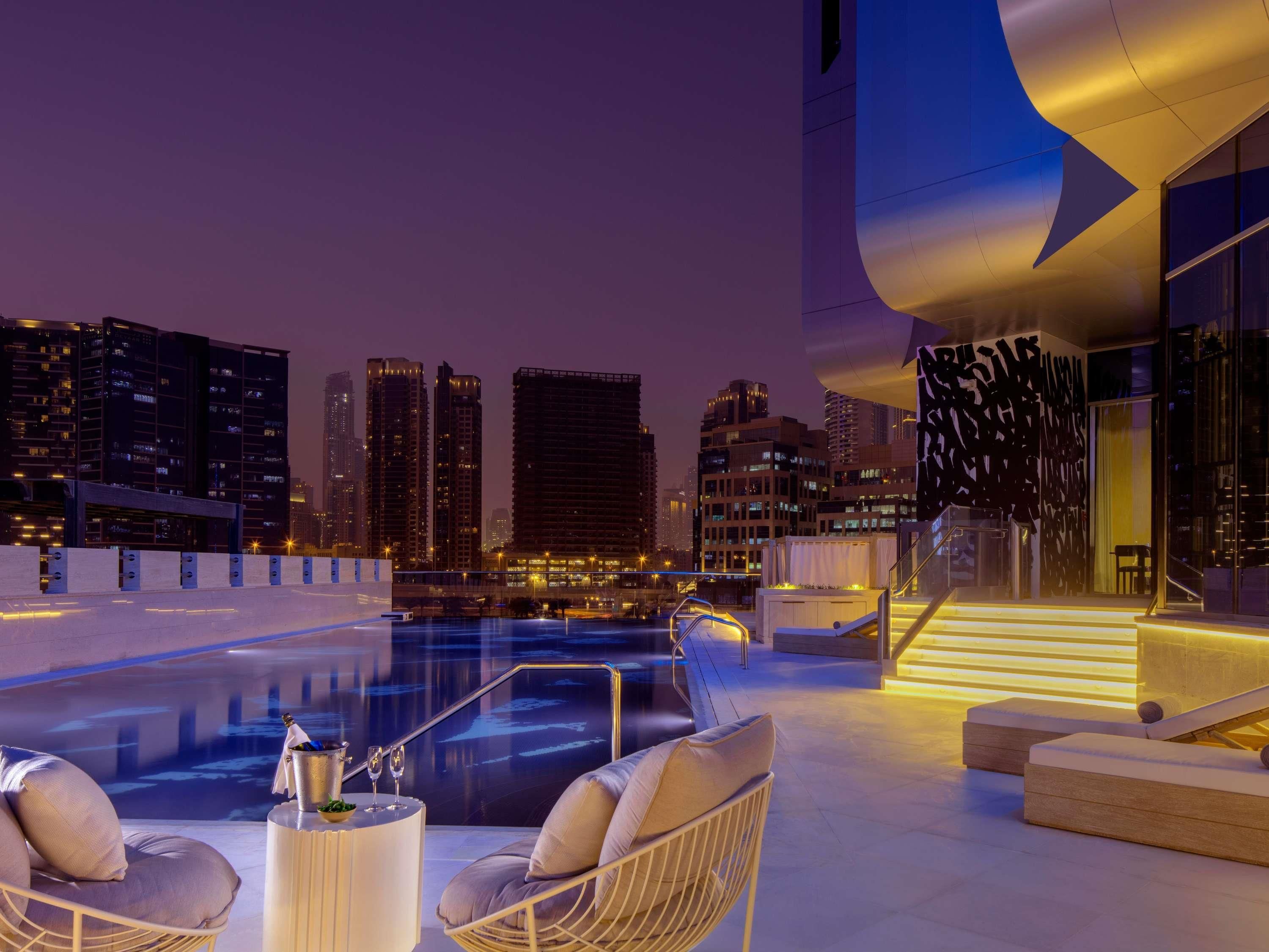 A rooftop pool area with lounge chairs and a city skyline view.