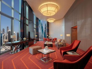 A modern hotel lobby with a large window offering a city view, a seating area with red chairs, and a reception desk. - Hyde Hotel Dubai (Dubai)