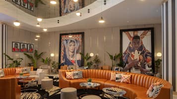Eine moderne Lobby mit einer gebogenen Ledersofa, runden Tischen und großformatiger Wandkunst.
