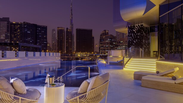 A rooftop pool area with modern seating and a city skyline view.