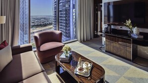 Habitación de hotel moderna con un amplio ventanal que ofrece vistas a la ciudad, un sofá cómodo, una mesita de centro con detalles y un televisor de pantalla plana.