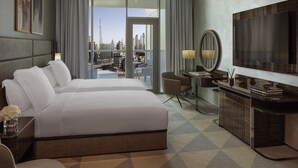 A hotel room with a large bed, a desk with a chair, a TV, and a view of a cityscape.