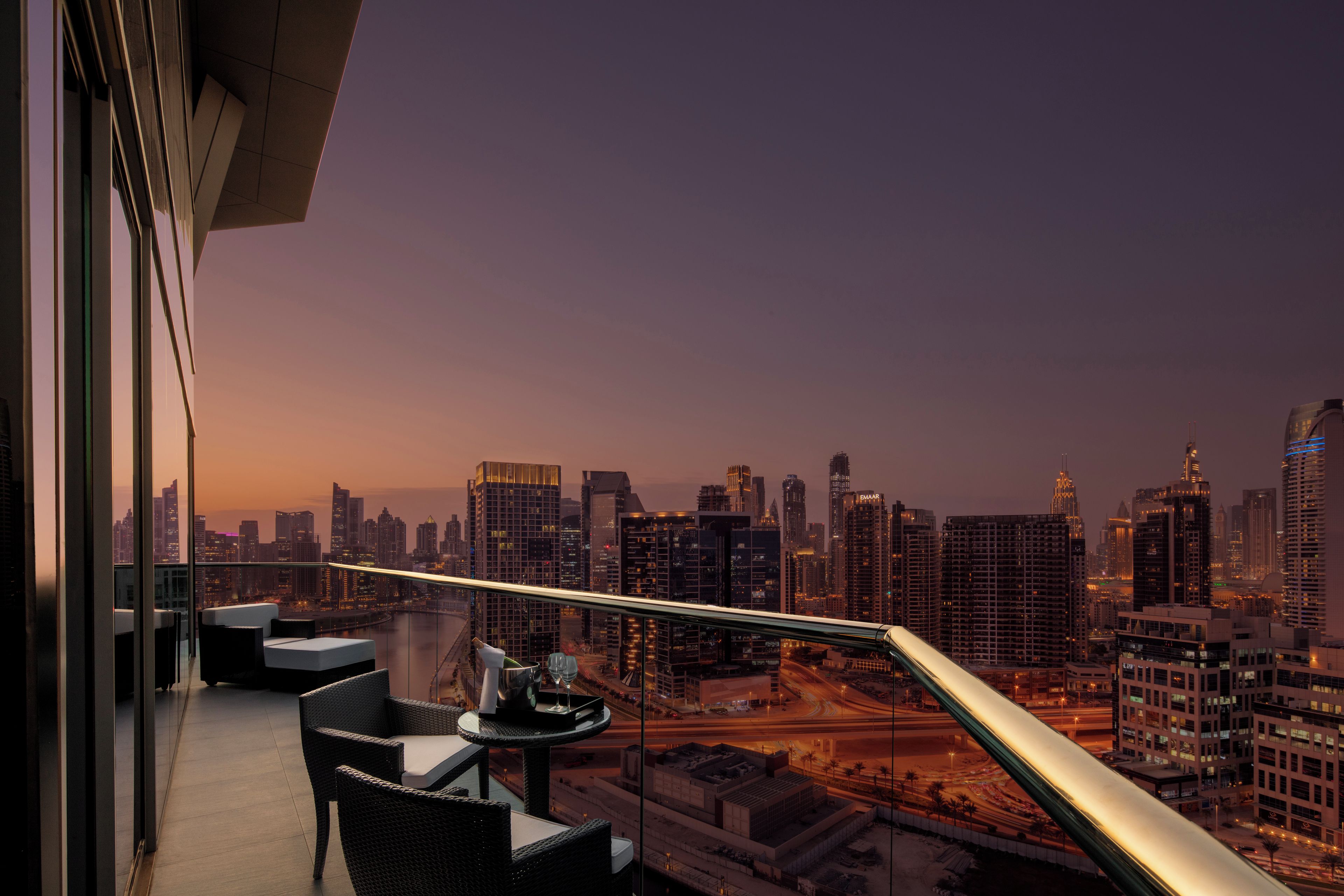 A balcony with a city view, a table with a glass, and wicker chairs.