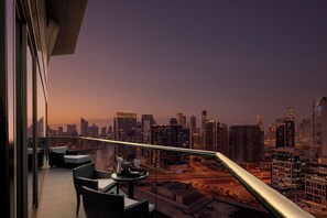 A balcony with a city view, a table with a glass, and wicker chairs. - Hyde Hotel Dubai (Dubai)