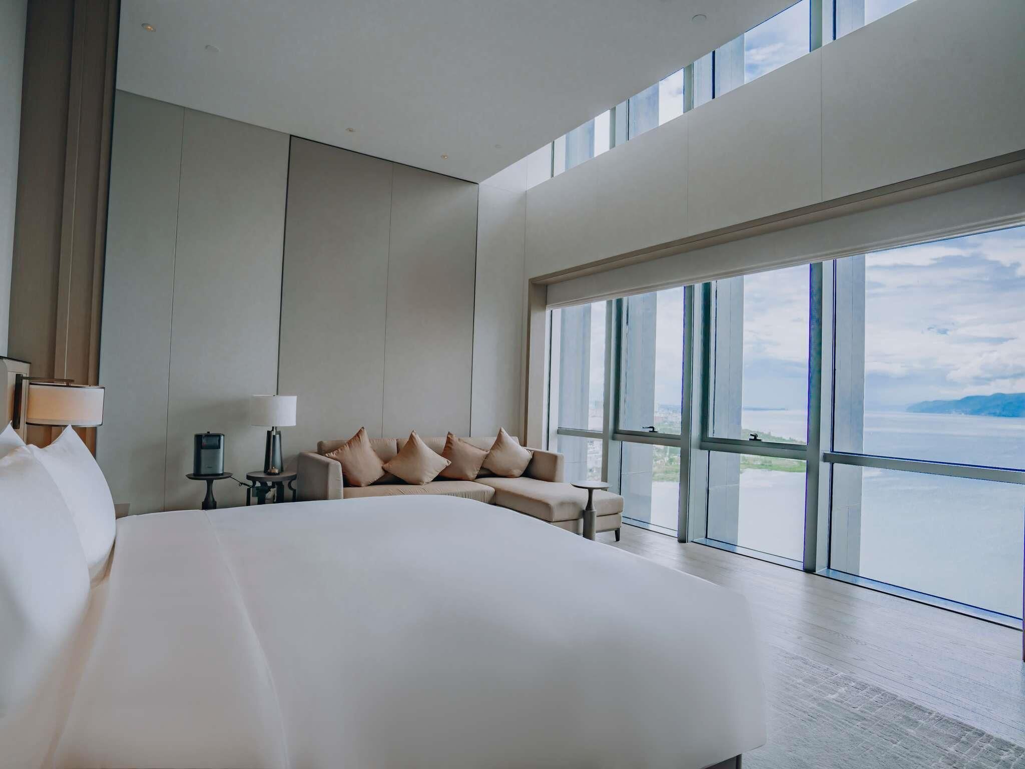 Una habitación de hotel moderna con una cama grande, un sofá, un escritorio y vista al mar.