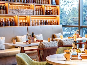 Un rincón acogedor con un banco de madera y sillas acolchadas, una mesa con una bandeja de tazas de café y una pared llena de frascos de vidrio.