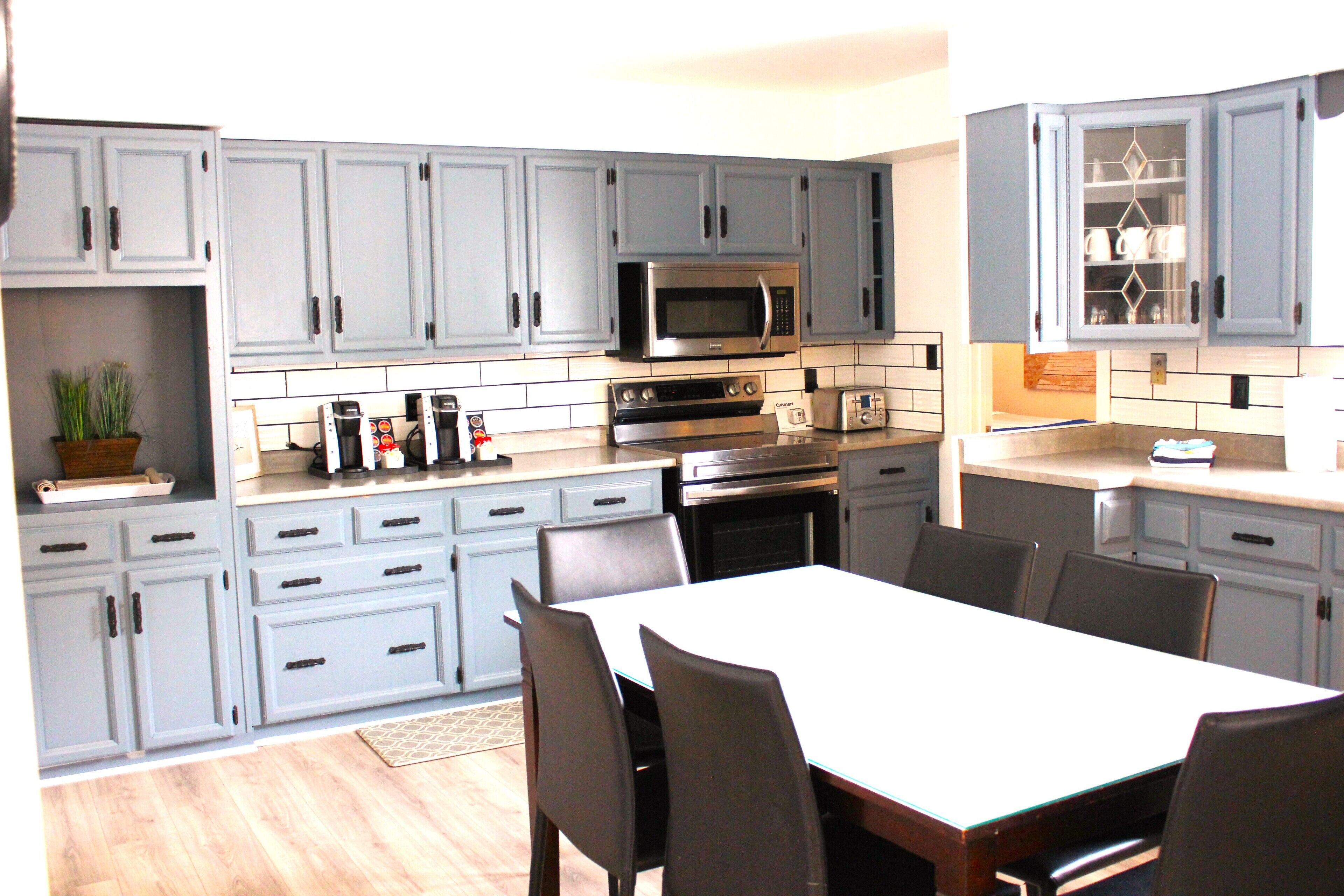 A modern kitchen with grey cabinets, a microwave, an oven, and a dining area with a table and chairs.