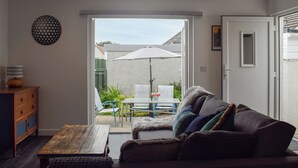 A living room with a sofa, a wooden coffee table, and a lamp. There is a sliding glass door leading to an outdoor area with a table and chairs. - 1 bedroom accommodation in St Andrews (St Andrews)