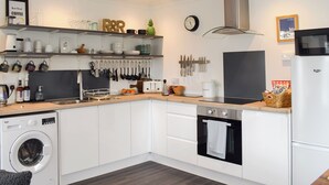 A modern kitchen with white cabinetry, a built-in washing machine, a stove, and a microwave. - 1 bedroom accommodation in St Andrews (St Andrews)