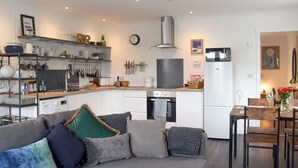 A modern kitchen with white cabinets, a built-in oven, and a large TV. There is a dining area with a wooden table and chairs. - 1 bedroom accommodation in St Andrews (St Andrews)