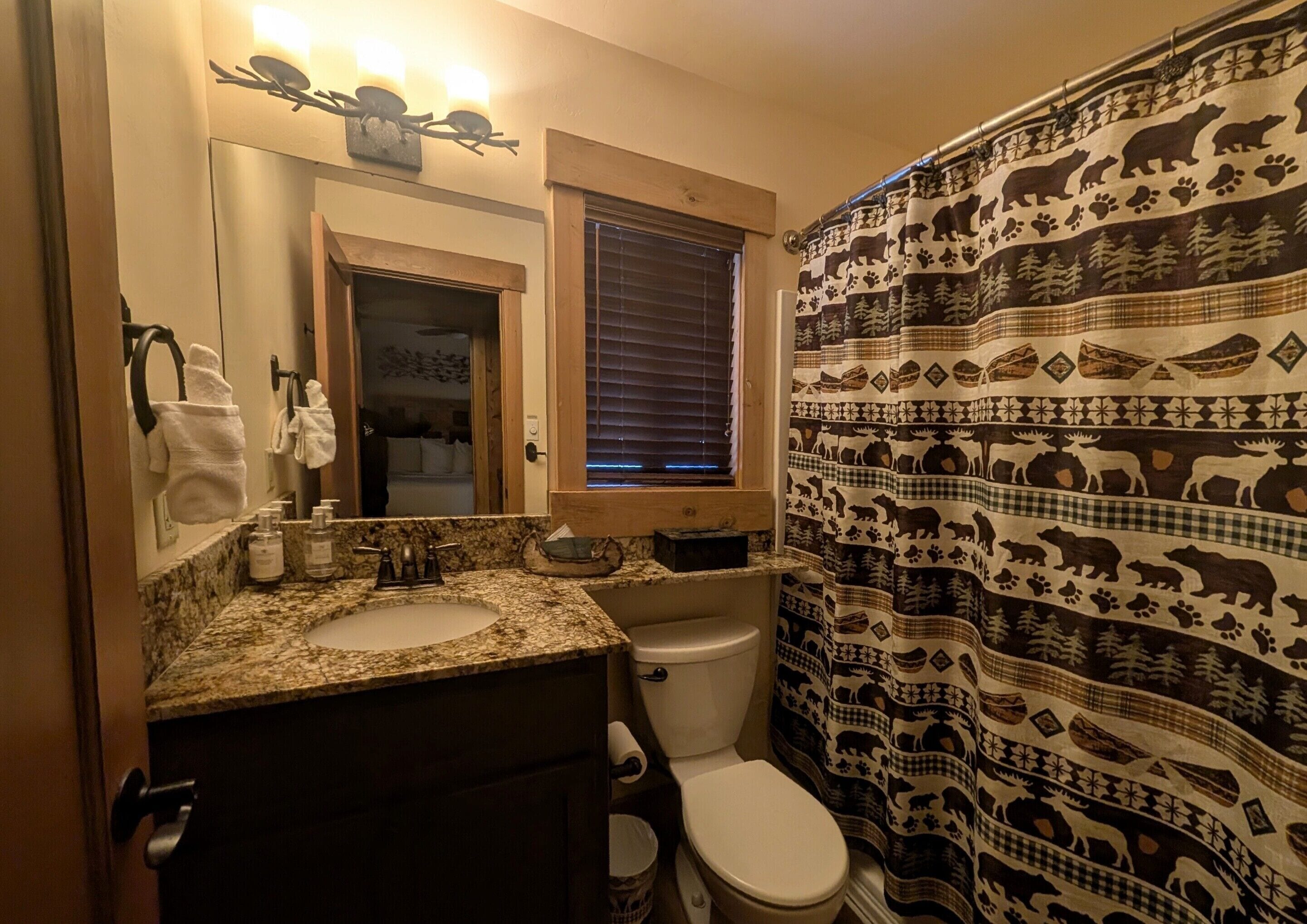 Casa de banho com lavatório bancada de granito, sanita e cortina de chuveiro com estampas de animais.