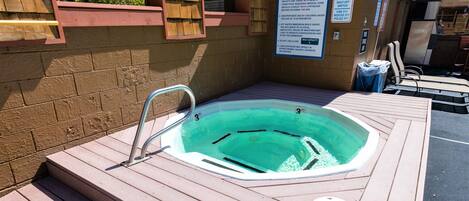 A hot tub with a caution sign, a wooden deck, and a poolside area with lounge chairs.
