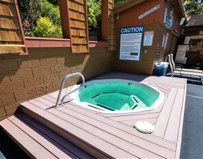 Een jacuzzi met een waarschuwingsbord, een houten terras en een zwembadgedeelte met ligbedden.