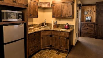 Una cocina con armarios de madera, microondas, refrigerador, lavamanos y un reloj en la pared.