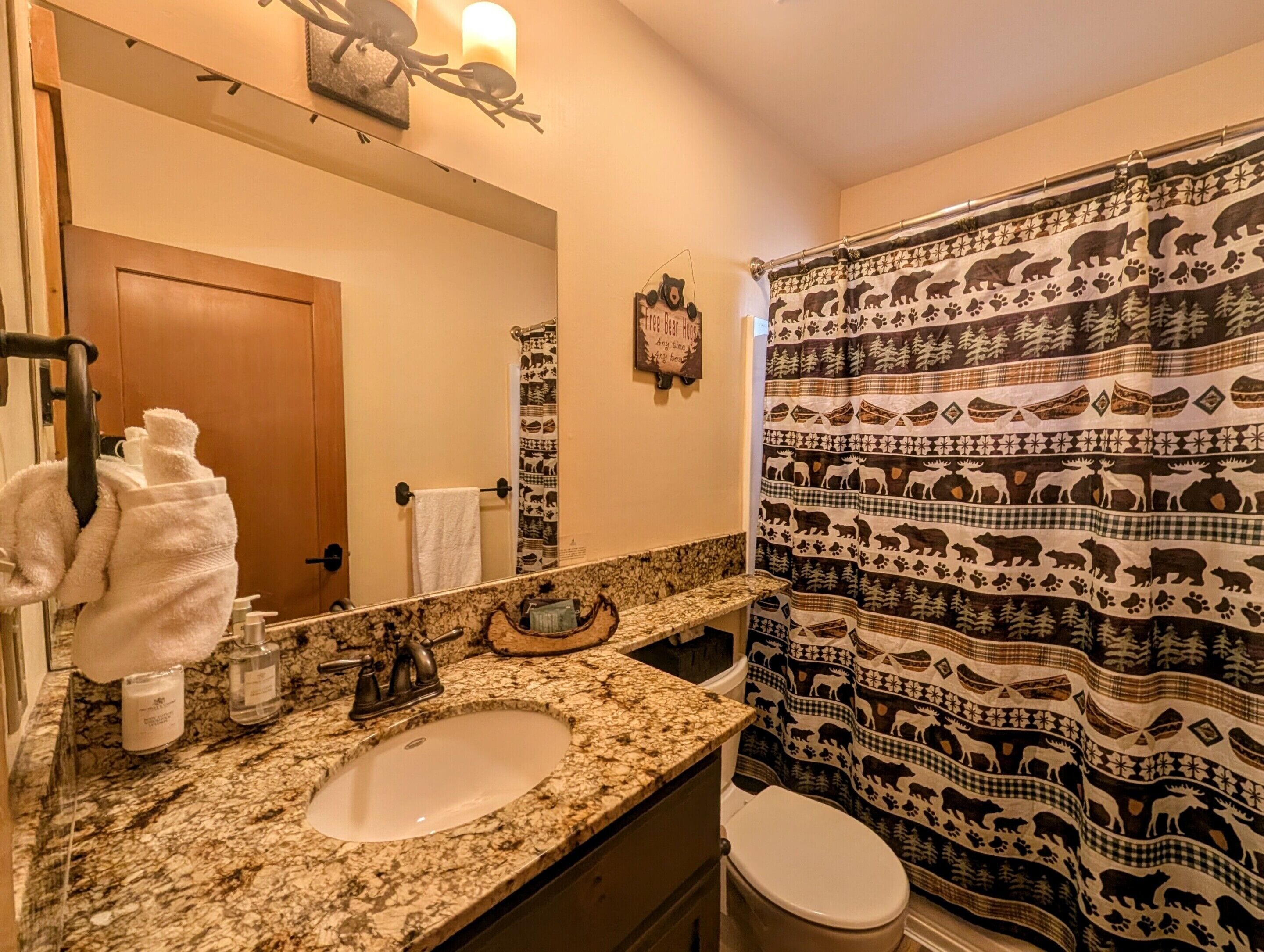 Baño con encimera de granito, lavamanos, inodoro, toallero y cortina de ducha con estampados de animales.