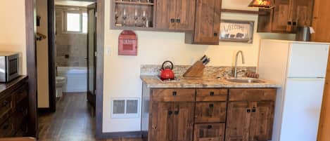 A kitchen with wooden cabinets, a granite countertop, a red kettle, and a white refrigerator.