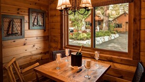 Un interior de madera con una mesa lista para comer, una ventana con vistas al exterior y una araña.