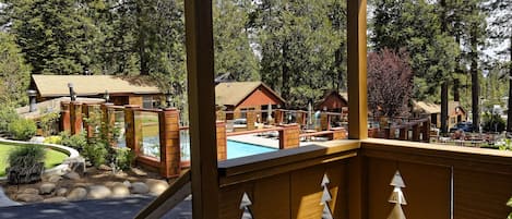 A wooden deck with a pool, surrounded by cabins and dense forest.