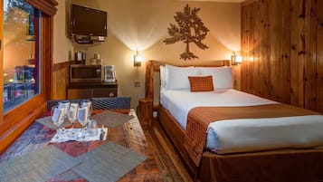 A hotel room with a bed, a desk with glasses and a coffee maker, a TV, and a wooden wall with a tree decoration.
