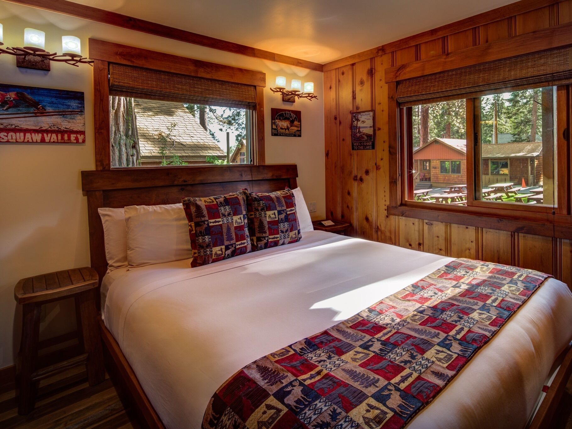 A large bed with a quilt, wooden walls, and a window with a view of a building outside.