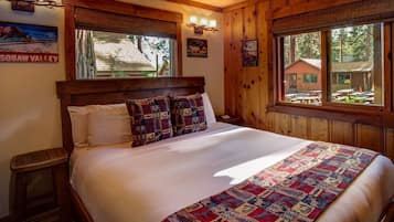 A large bed with a quilt, wooden walls, and a window with a view of a building outside.