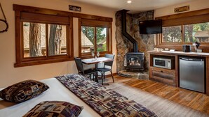 Una habitación acogedora con una cama, una mesa con sillas, una pared de piedra, una chimenea, un televisor y una zona de cocina.