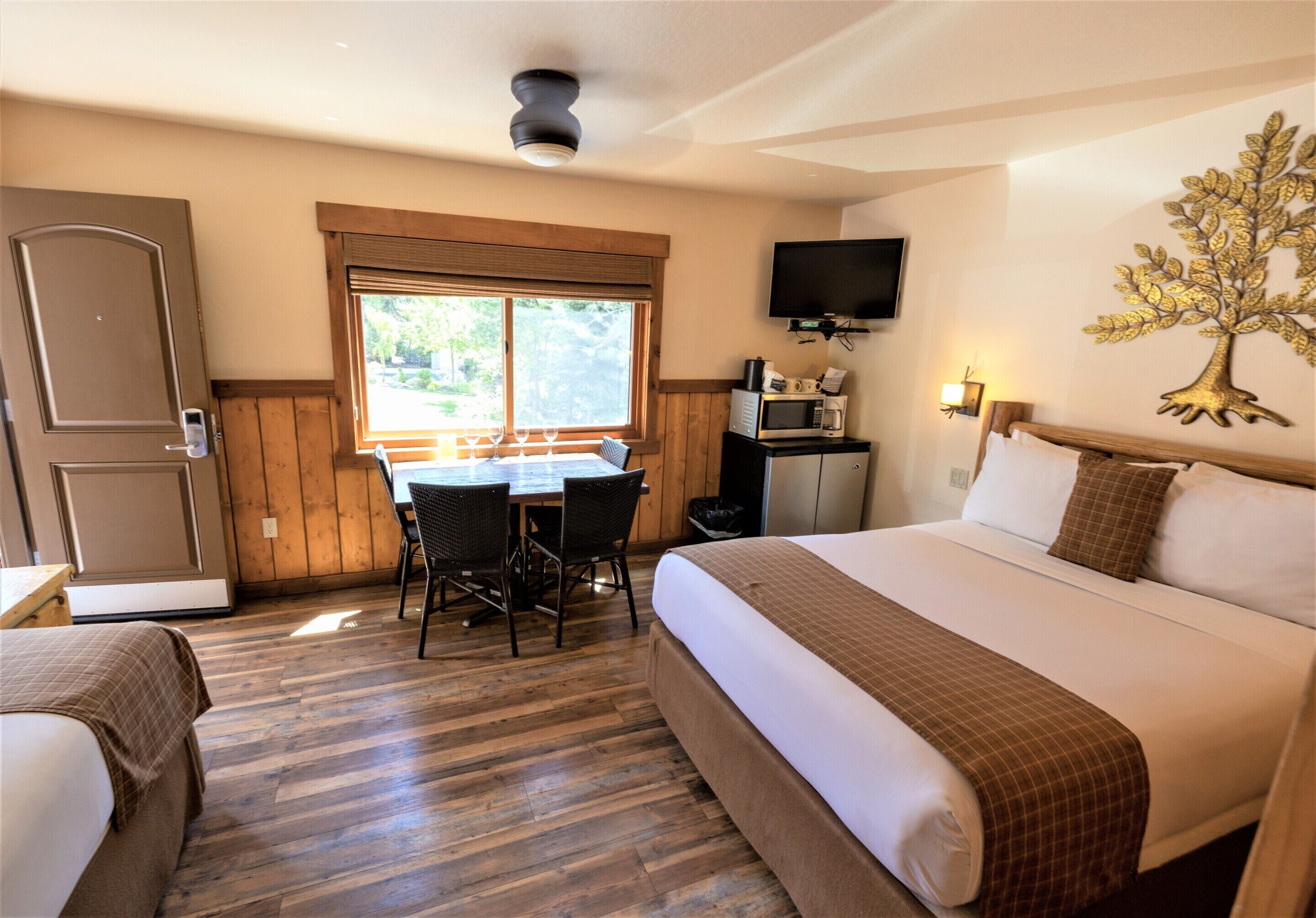 Ein Hotelzimmer mit einem großen Bett, einem Schreibtisch mit Stuhl, einem Fernseher und einem Fenster mit Blick auf Grünflächen.