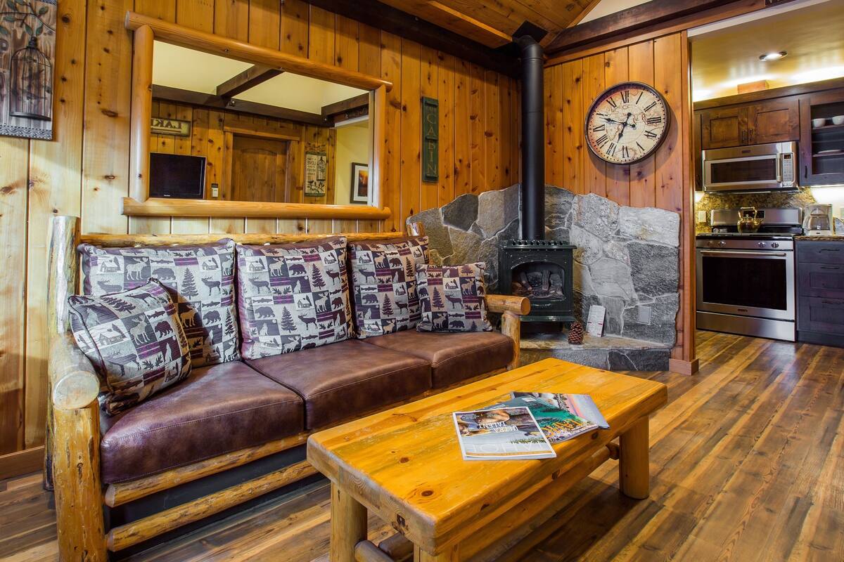 Ein gemütliches Blockhaus mit Kamin aus Stein, Holzwänden, einer Ledersofa und einem Holztisch.