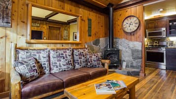 Un interior de cabaña acogedor con chimenea de piedra, paredes de madera, un sofá de cuero y una mesa de centro de madera.