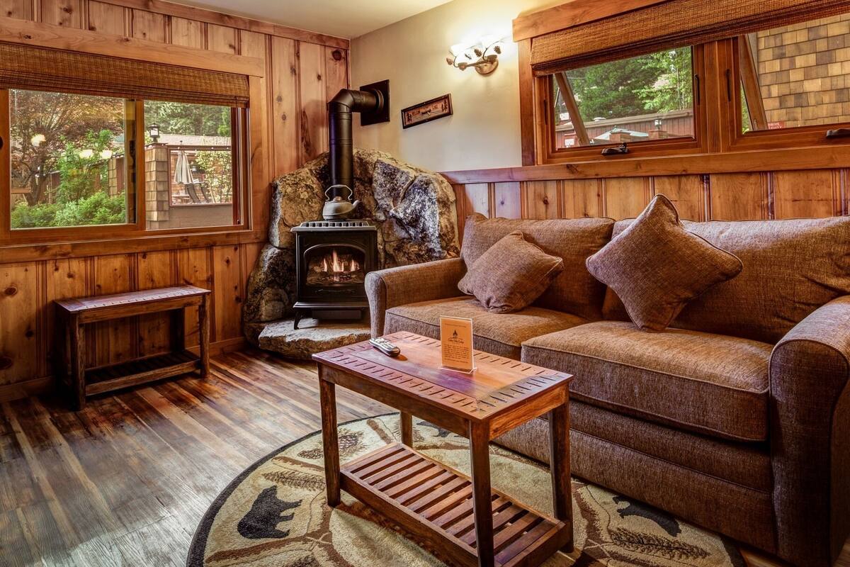 Ein gemütliches Blockhäuschen-Interieur mit Kamin aus Stein, Holzwänden, einer Couch und einem kleinen Tisch.