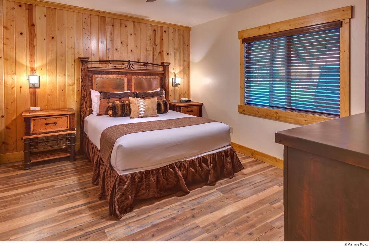 Ein Schlafzimmer mit Holzwänden, einem Bett, Nachttischen, einem Deckenventilator und einem Fenster mit Jalousien.