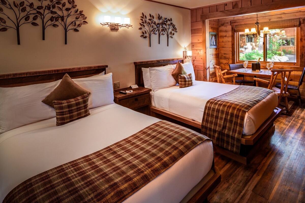 Ein Hotelzimmer mit zwei Betten, Holz-Kopfteilen, einem Esstisch mit Stühlen und Blick ins Freie durch ein Fenster.