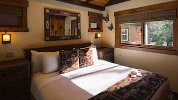 Une chambre avec un plafond en bois, un grand lit avec une literie à motifs, une table de chevet, un miroir et une fenêtre donnant sur un paysage verdoyant.