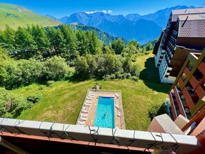 A pool with lounge chairs, surrounded by greenery and mountains in the background.