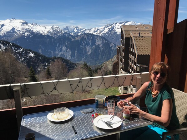 A balcony with a table set for two, overlooking snow-capped mountains.