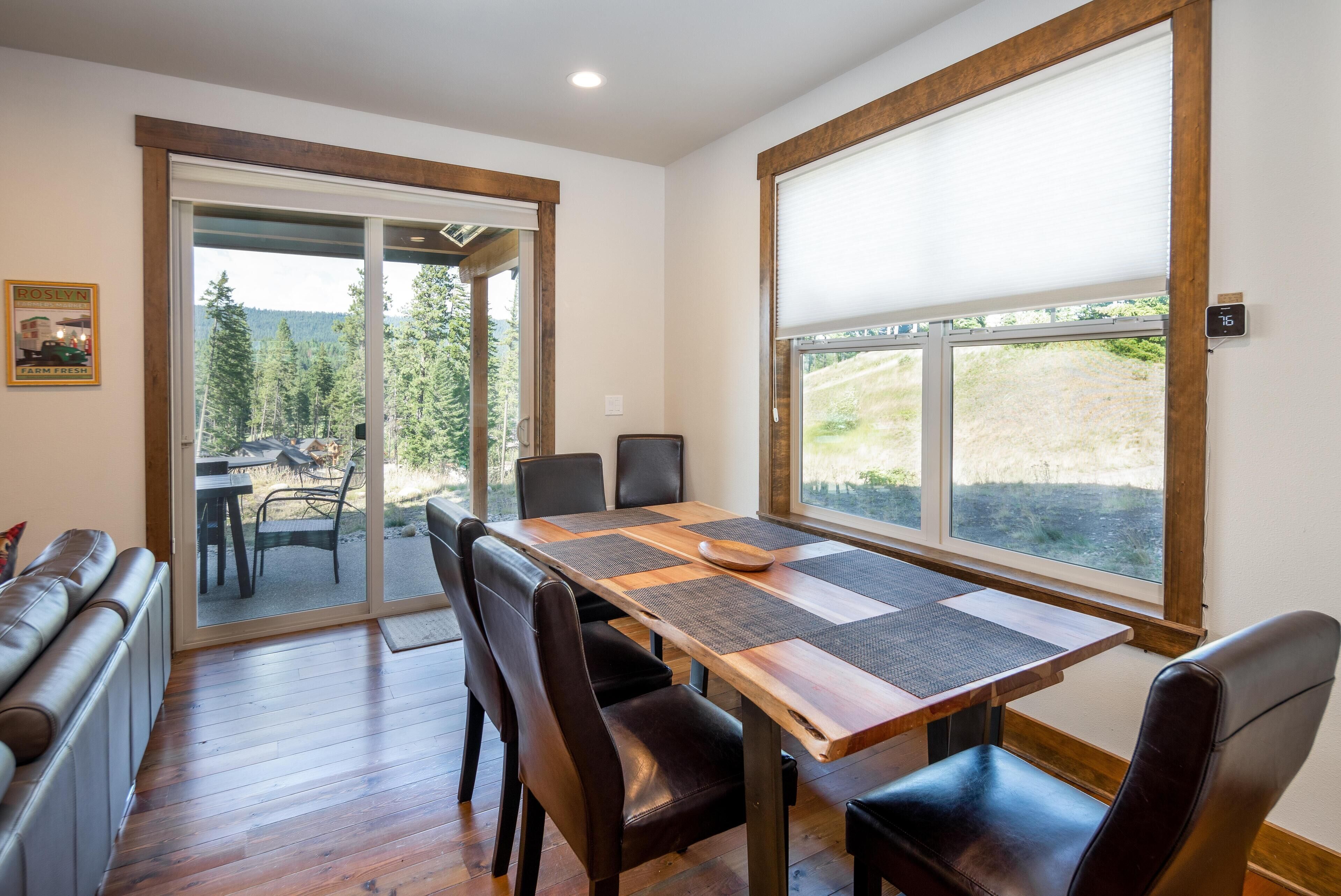 A dining area with a wooden table, black chairs, and a view of a forest through large windows.